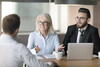 a woman and a man talk to another man at a table with their laptop open